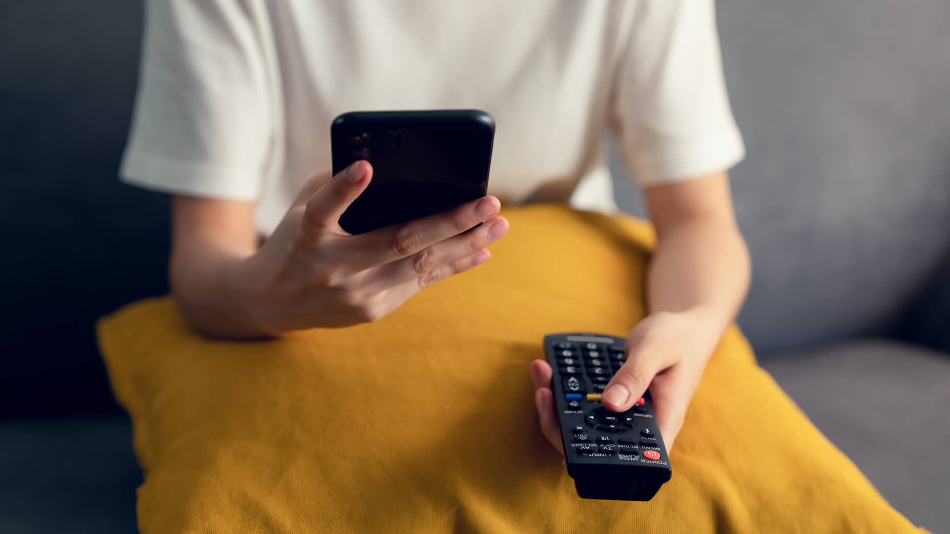 Persona usando su smartphone mientras cambia de canal su tv con internet con paquete básico de axtel