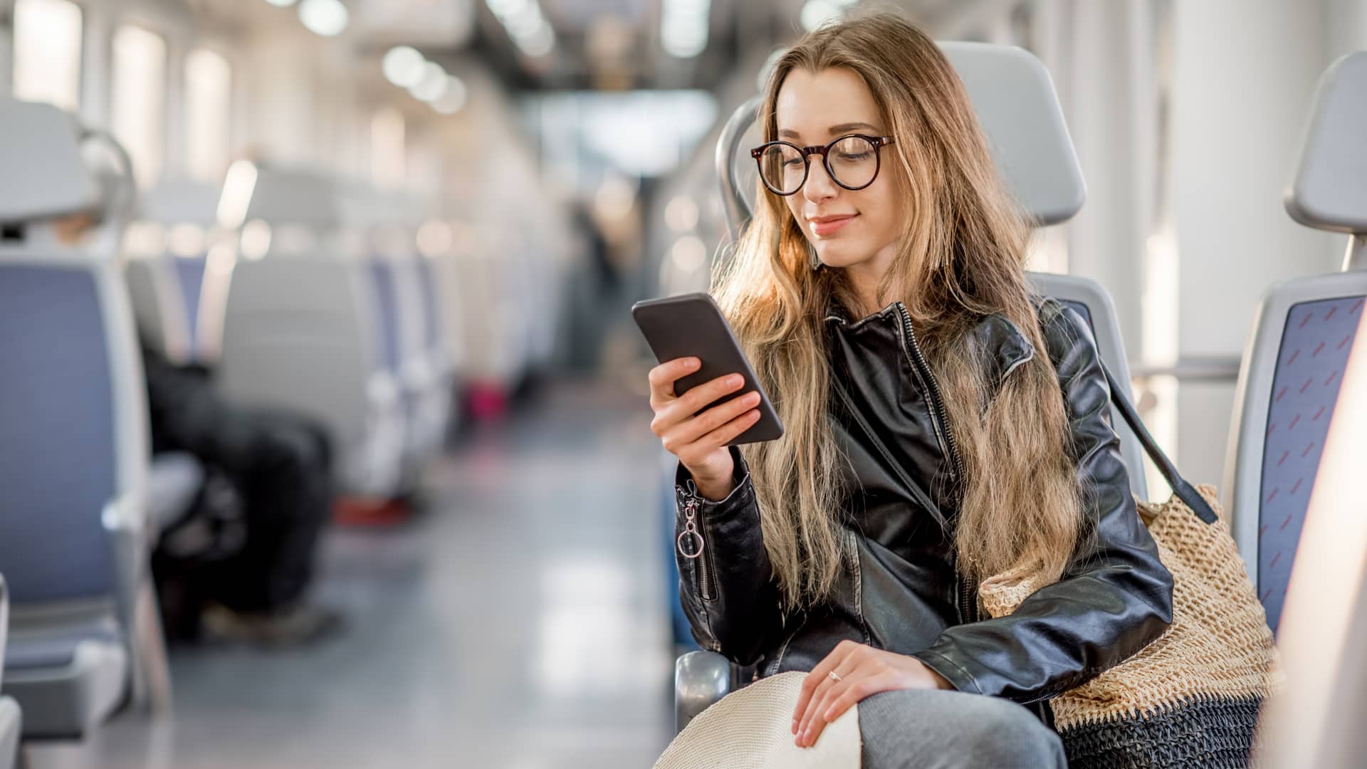 Mujer hermosa con gafas chequea su celular en un tren mientras comprueba su coste de roaming al salir del país