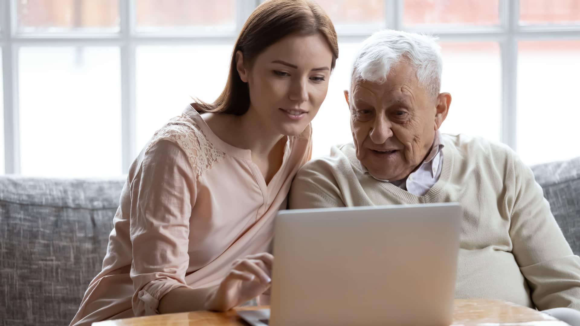 una joven ayudando a su abuelo con el ordenador a realizar la recarga como clientes de sky