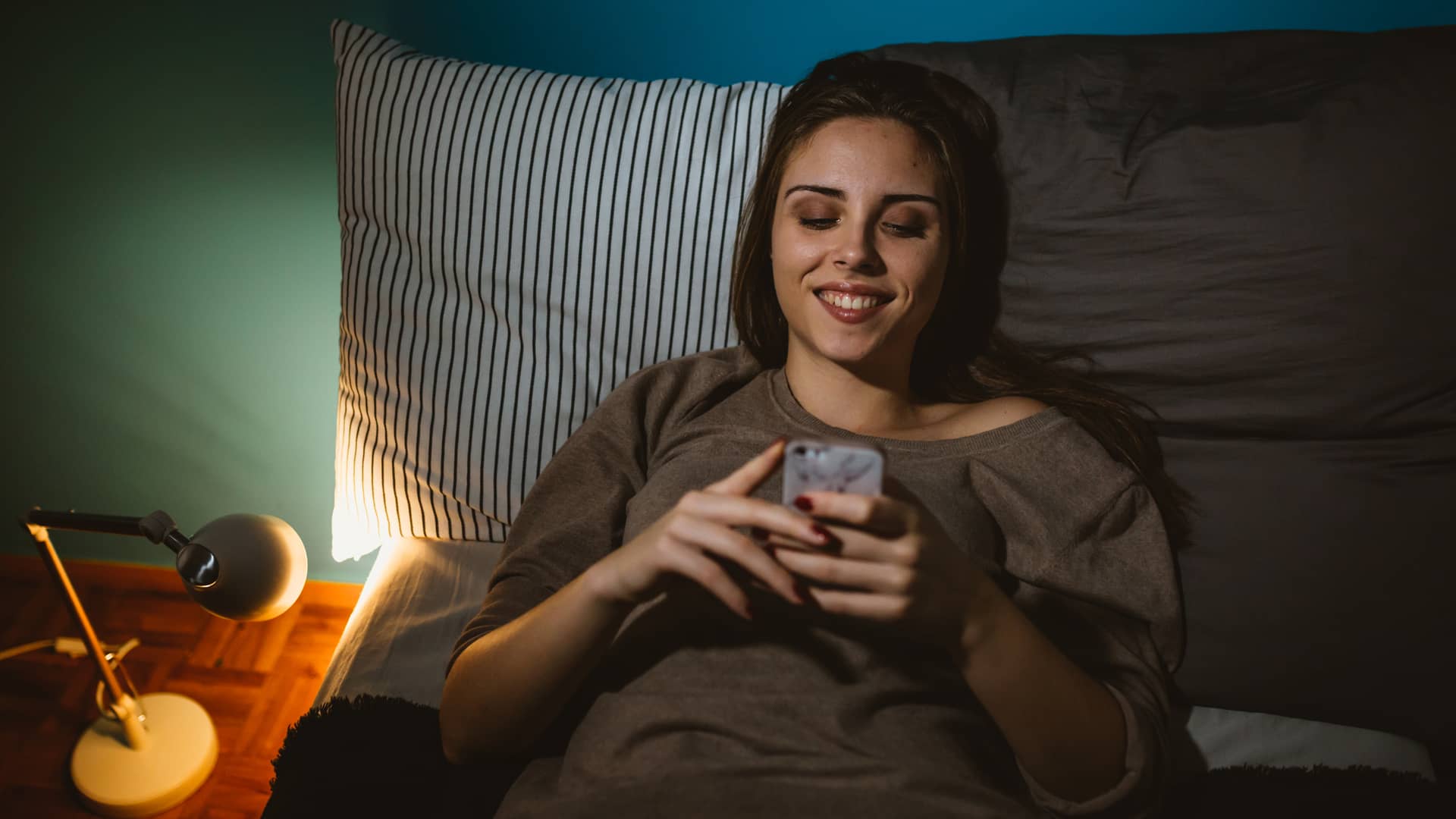 joven tumbada en la cama con su celular revisando su saldo con telmex en la app