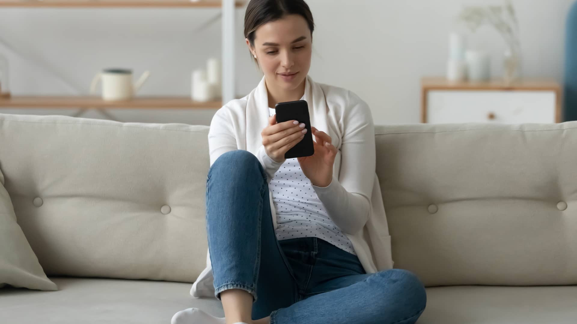mujer en el sofa de su casa que va a mandar un sms para saber el numero de unefon